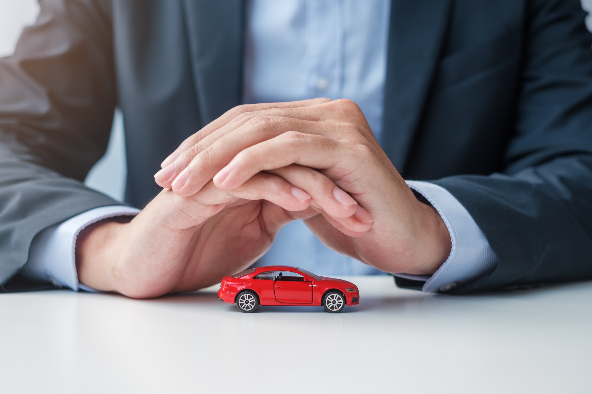 Businessman hand cover or protection red car toy on table. Car insurance, warranty, repair