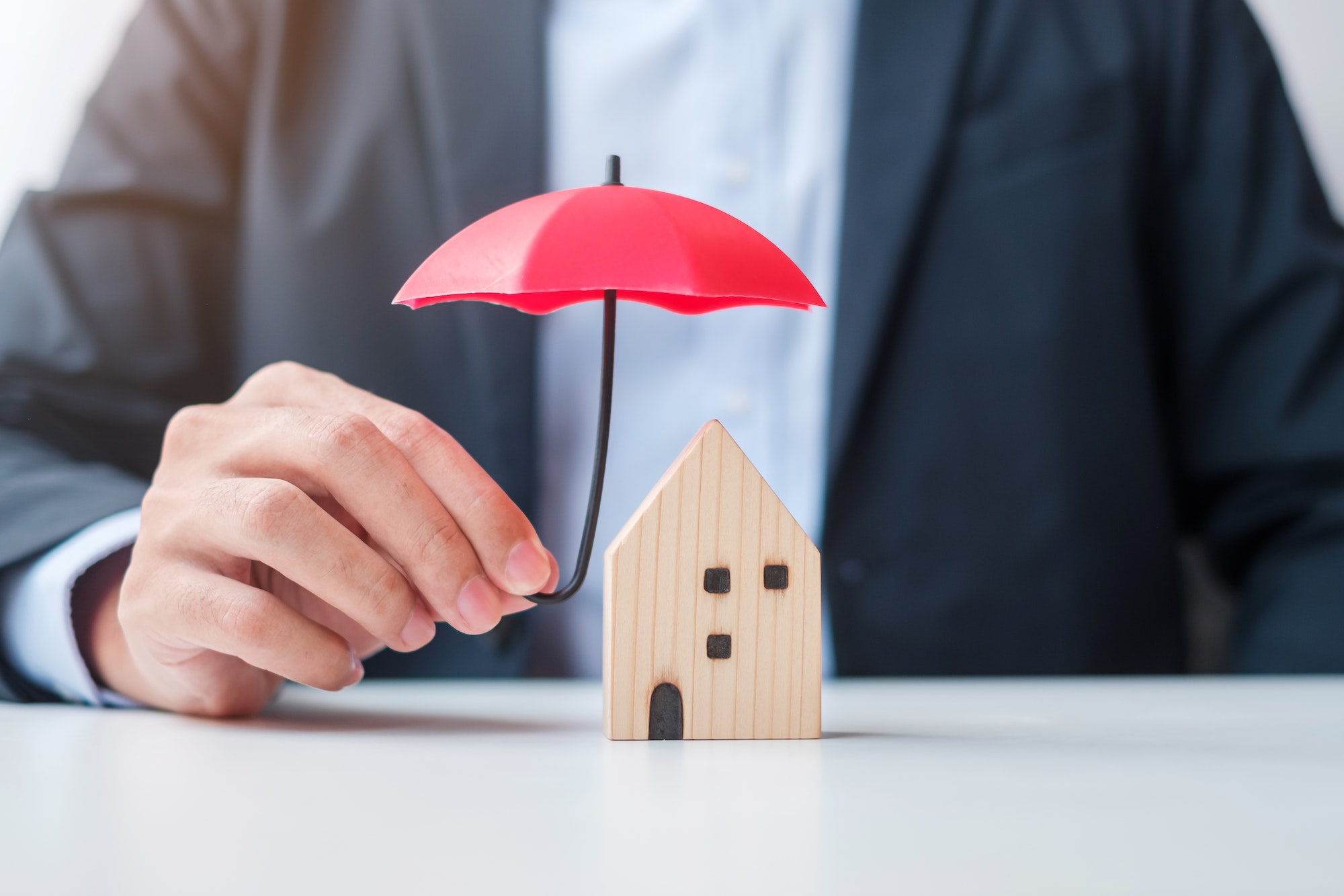 Businessman hand holding red Umbrella cover wooden Home model. real estate, insurance and property