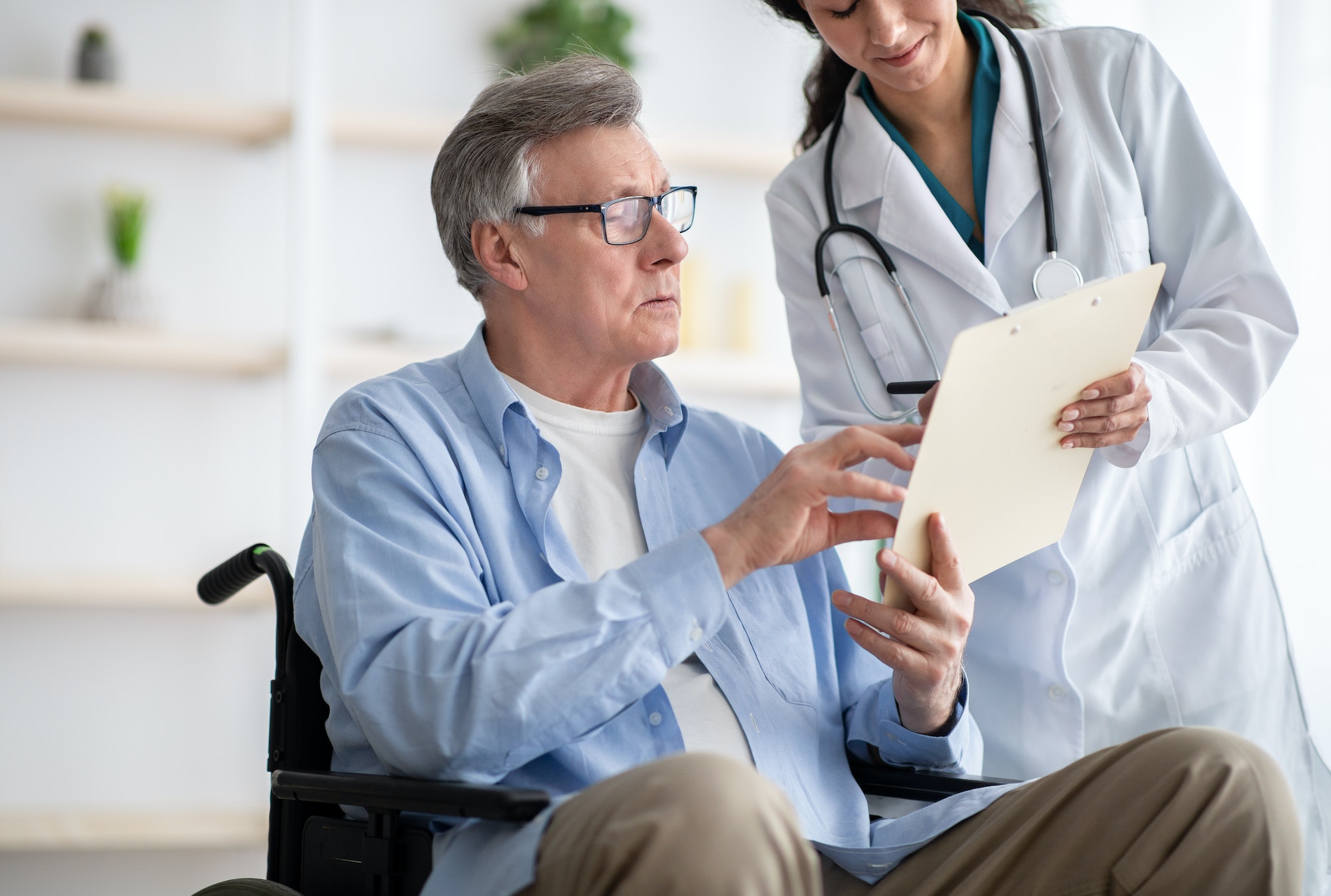 Positive female doctor offering disabled elderly man to sign insurance contract at home