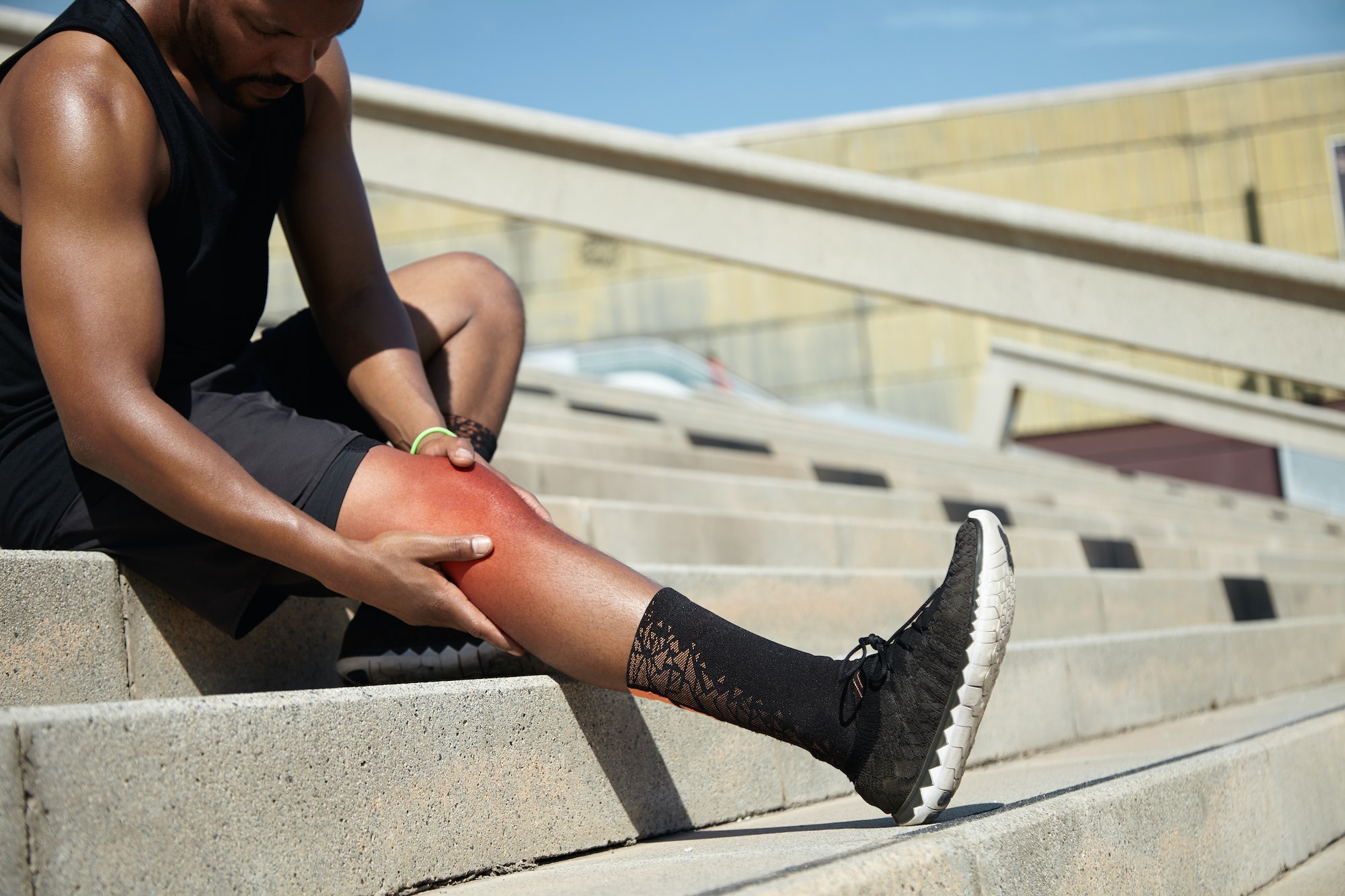 Young sportsman with strong athletic legs holding knee after suffering ligament injury during runnin