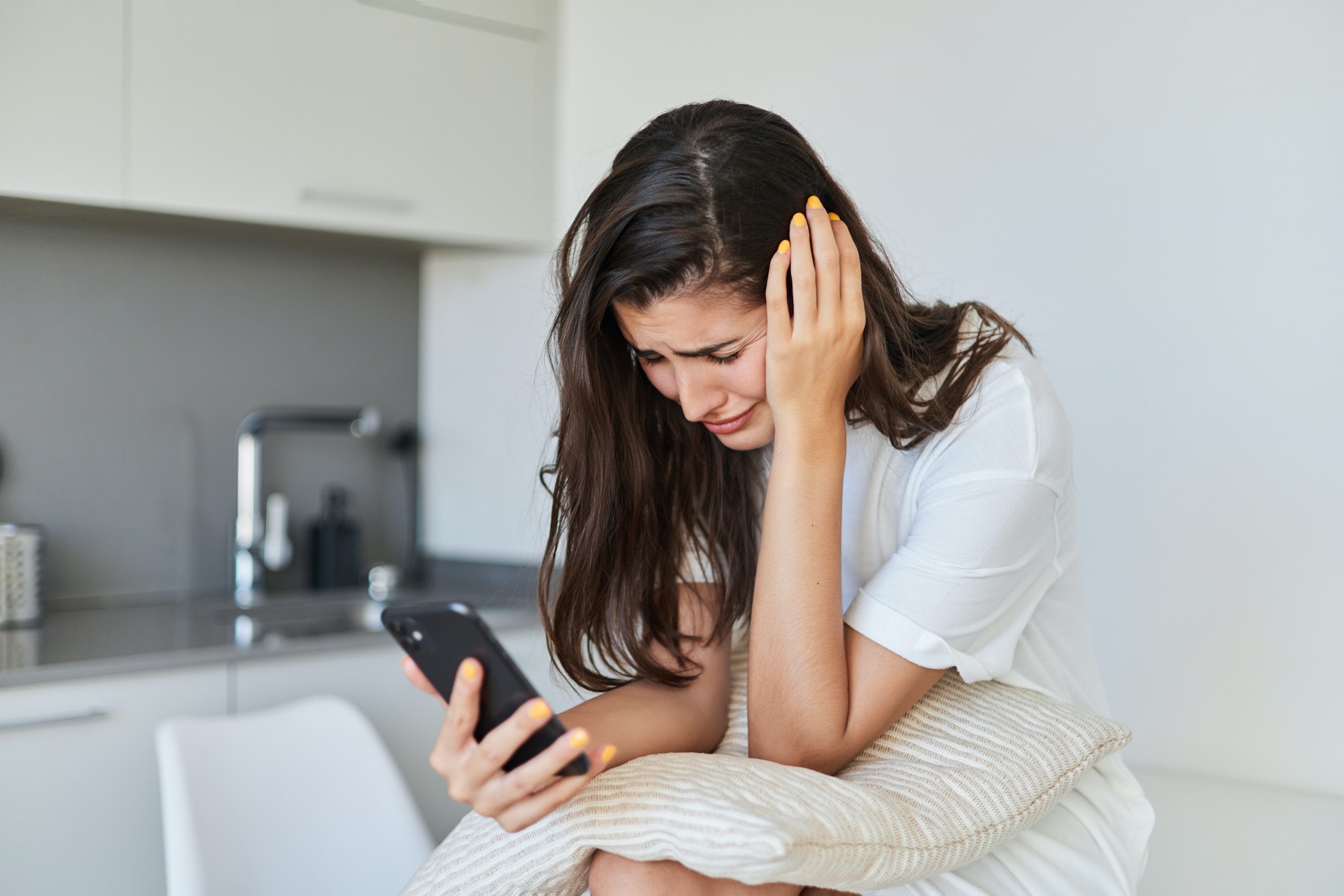 Sad young woman with depression using her mobile phone at home